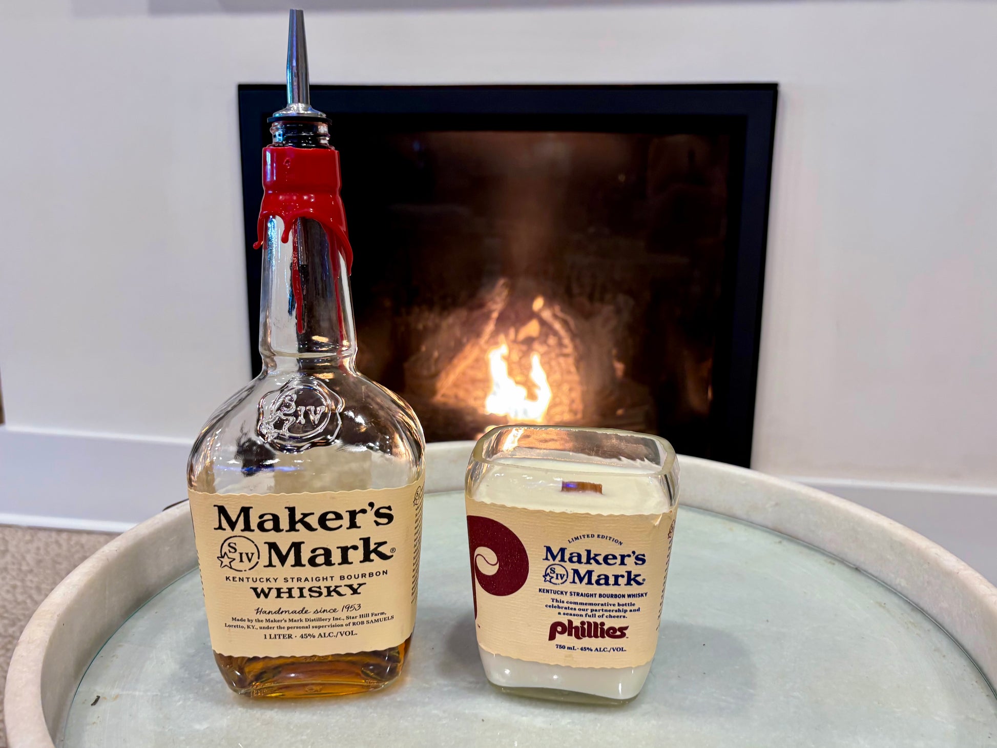 Bottle and candle of Maker's Mark on a surface with a fireplace in the background