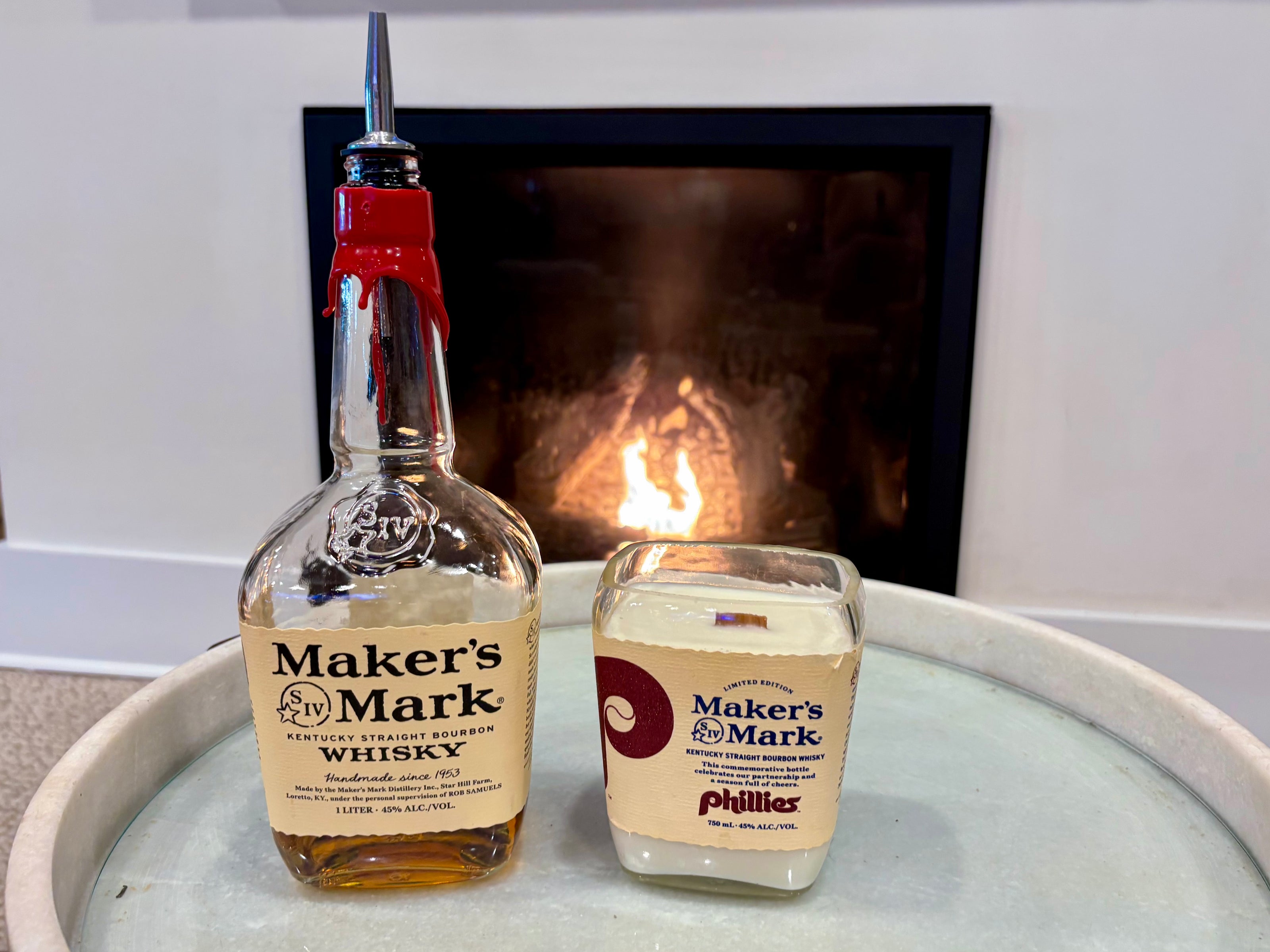 Bottle and candle of Maker's Mark on a surface with a fireplace in the background