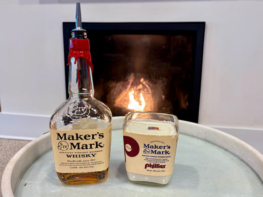 Bottle and candle of Maker's Mark on a surface with a fireplace in the background
