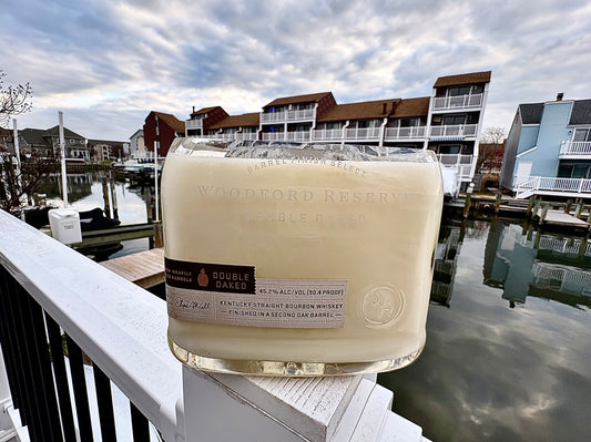 Glass bottle of Woodford Reserve bourbon on a railing with a waterfront and buildings in the background